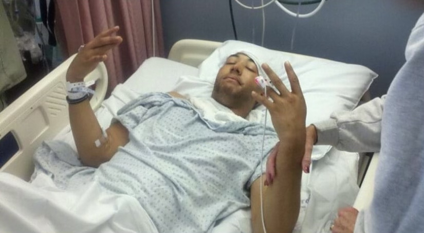 Injured man in hospital bed with bandages and monitors (Cameron McFadden) after being the victim of a shooting in Oakland, California.